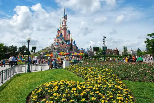 Disneyland Paris castle with colorful flowers and crowds of people.