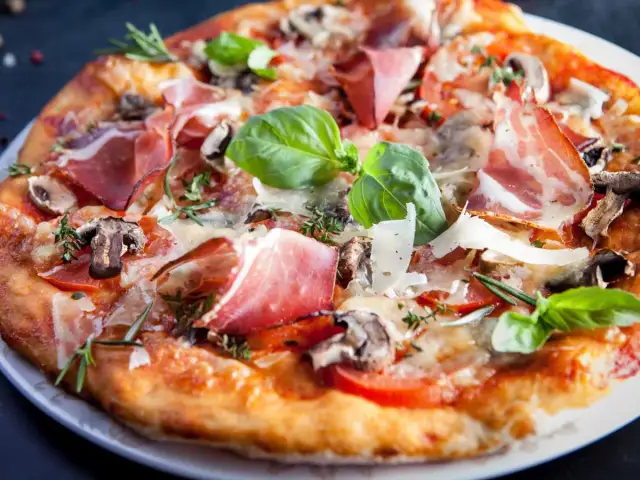 Pyszna pizza parma z szynką, pieczarkami, pomidorami i bazylią, posypana parmezanem.