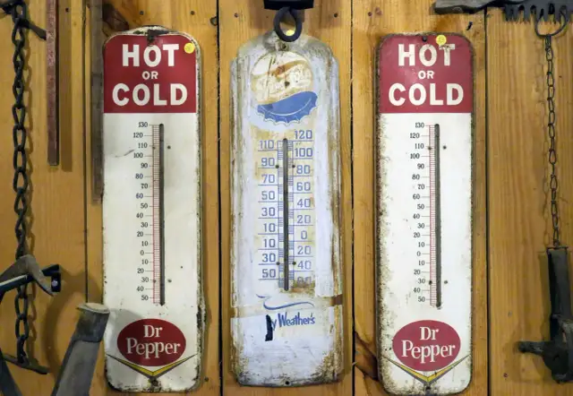 Trzy stare termometry wiszą na drewnianej ścianie. Dwa z nich reklamują Dr Pepper, jeden pokazuje "Ay Weather's". Idealne do monitorowania temperatury w biurze.