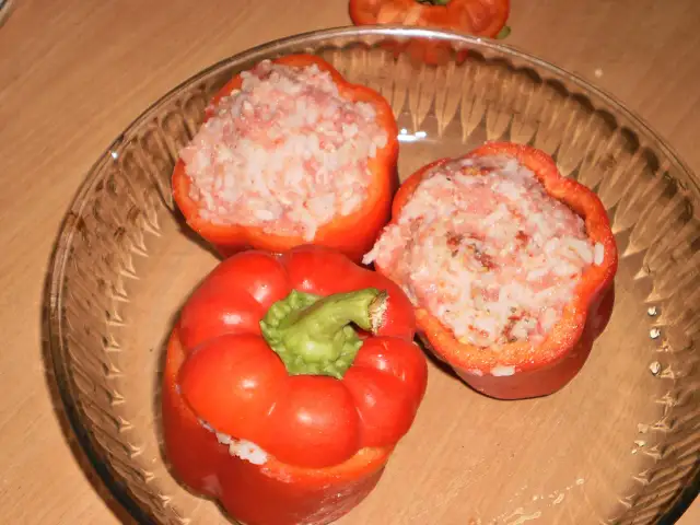 Trzy czerwone papryki faszerowane surowym mięsem mielonym i ryżem, gotowe do pieczenia.