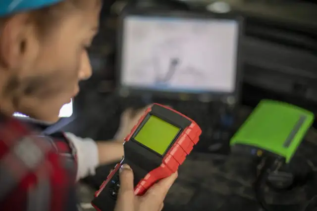 Mechanik z urządzeniem diagnostycznym i laptopem w tle.