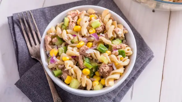 Ein köstlicher nudelsalat mit thunfisch, garniert mit Mais, Gurken und roten Zwiebeln, bereit zum Genießen.