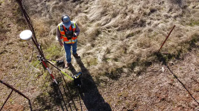 Geodeta w kamizelce odblaskowej z aparaturą GPS przy płocie.