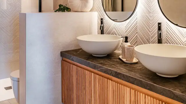 Modernos cuartos de baños con lavabos sobre encimera, grifería negra y detalles en madera.