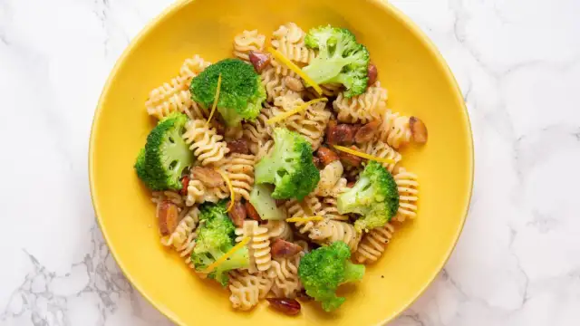 Macarrones con brócoli, trozos de salchicha y ralladura de limón en un plato amarillo.