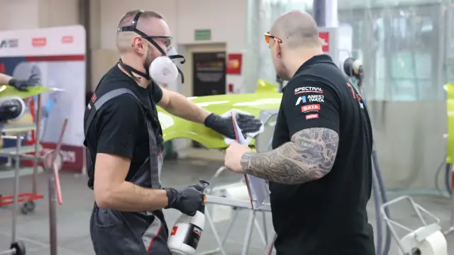 Dwóch mężczyzn w maskach i rękawiczkach pracuje nad zielonym elementem, sprawdzając, czy na podkład epoksydowy można kłaść lakier.
