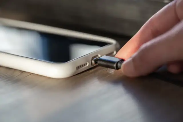 Une main insère un câble dans la connectique d'un iPhone 13, prêt à le recharger.