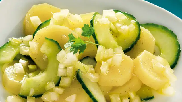 Ein appetitlicher Kartoffelsalat mit Gurken, verfeinert mit Zwiebeln und Petersilie.