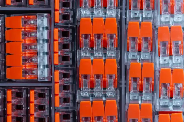 Zbliżenie na pomarańczowe złącza elektryczne w przezroczystych obudowach, ułożone w rzędy.