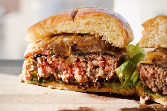 Przekrojony, soczysty burger z karmelizowaną cebulą i sałatą na desce.