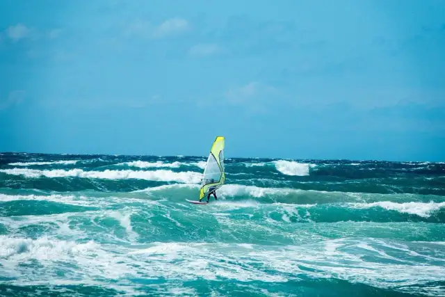 Windsurfer na wzburzonym, turkusowym morzu pod błękitnym niebem.