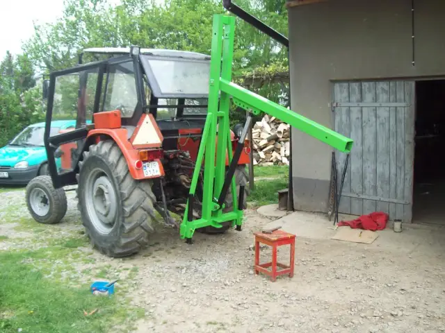 Czerwony traktor z zamontowanym zielonym ładowaczem TUZ przed budynkiem gospodarczym.