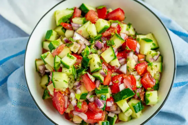 Frischer Tomaten-Gurken-Salat mit roten Zwiebeln und Kräutern, serviert in einer Schüssel.