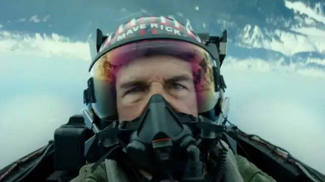 Tom Cruise jako Maverick w hełmie z napisem "MAVERICK" w filmie Top Gun: Maverick. Intensywne spojrzenie pilota w kokpicie myśliwca.