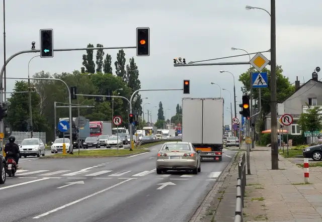 Kierowca srebrnego sedana decyduje się na przejazd na żółtym świetle, mimo że sygnalizator obok świeci na czerwono.