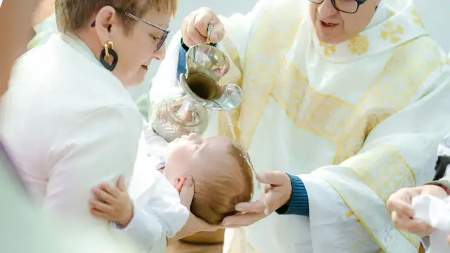 Chrzest dziecka: ksiądz polewa głowę niemowlęcia wodą z kropielnicy.