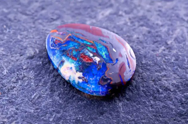 Ein faszinierender Edelstein aus Australien, ein Boulderopal, zeigt ein lebendiges Farbspiel aus Blau, Rot und Orange auf dunklem Grund.