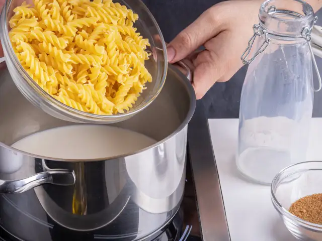 Eine Hand schüttet Spiralnudeln in einen Topf mit Milch. Zutaten für milch nudeln.