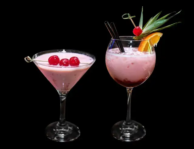 Dwa różowe drinki, jeden w kieliszku martini z wiśniami, drugi w kieliszku typu goblet z owocami. Zastanawiasz się, ile kalorii ma wódka smakowa?