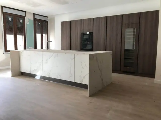 Cocinas modernas con barra central de mármol y gabinetes oscuros.