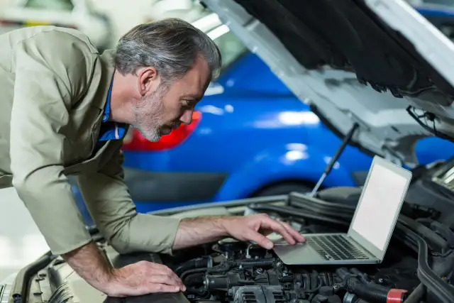 Mechanik z laptopem przy otwartej masce samochodu.