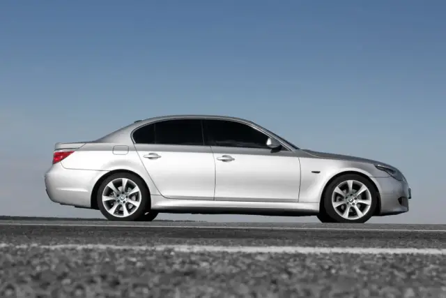 Srebrne BMW 5 E60 na tle błękitnego nieba, zaparkowane na drodze.