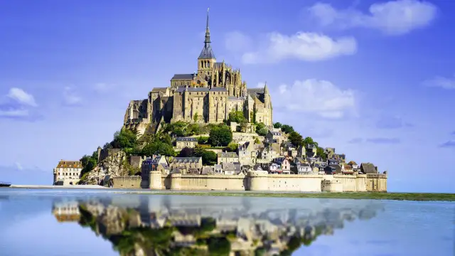 Opactwo Mont Saint-Michel, jeden z najpiękniejszych miejsc we Francji, odbija się w spokojnej wodzie.