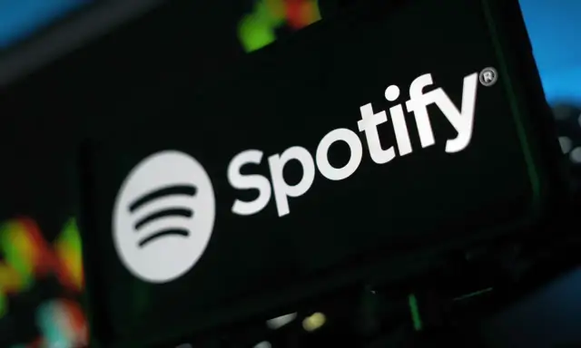 Logo Spotify na ciemnym tle, z rozmytymi kolorowymi światłami w tle.