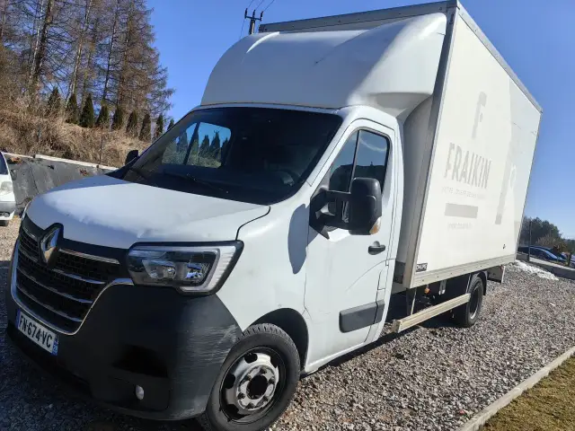 Biały bus z zabudową typu bliźniak, zaparkowany na żwirowym podjeździe.