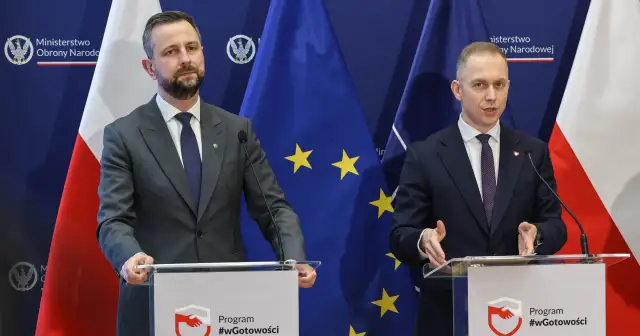 Dwóch mężczyzn w garniturach przemawia za mównicami. Tło stanowią flagi Polski i UE. Tematem dyskusji mogło być to, jak rządy PiS zmieniły strukturę polskiego wojska.