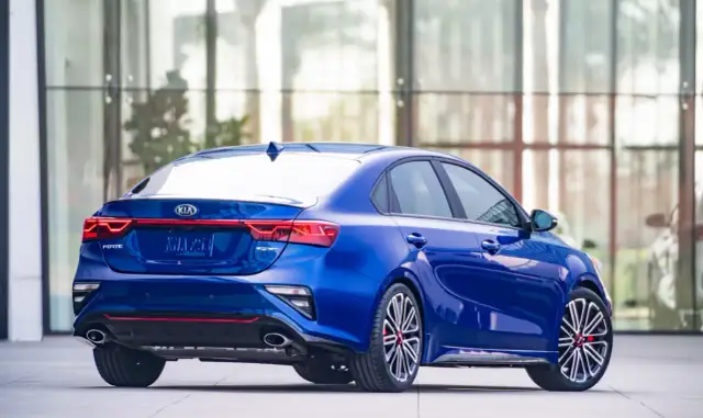 Niebieskie Kia Forte GT z czerwonymi akcentami, zaparkowane przed nowoczesnym budynkiem.