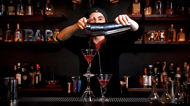 Barman nalewa czerwony drink z shakera do kieliszka martini.