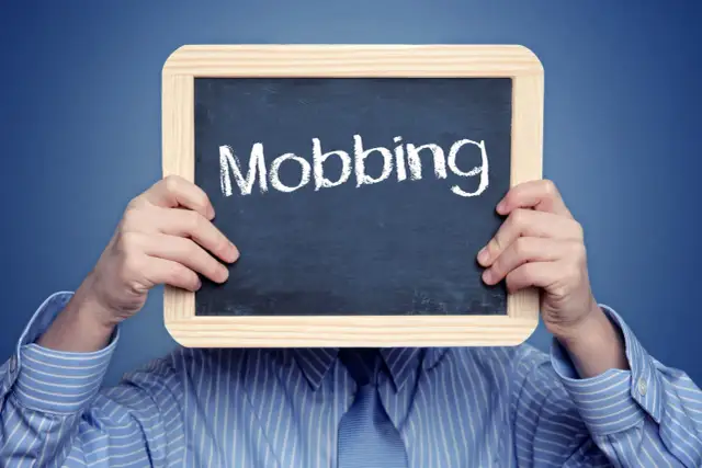 Osoba w koszuli trzyma tabliczkę z napisem "Mobbing". To symbol naruszenia dóbr osobistych i nękania w pracy.