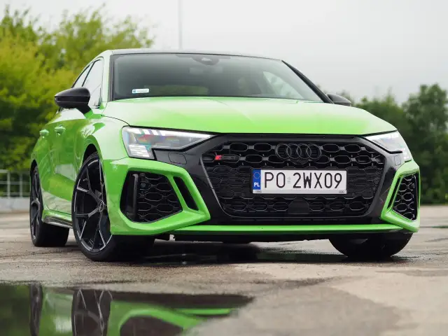 Jaskrawozielone Audi RS3 Sedan z czarnymi felgami stoi na mokrej nawierzchni, odbijając się w kałużach.