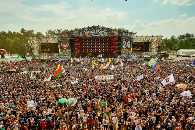 Tłum ludzi na festiwalu Poland Rock, gdzie jest scena i ekrany. Wszędzie flagi i słońce.