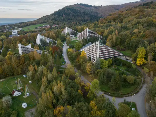 Widok z lotu ptaka na sanatoria o trójkątnej architekturze w otoczeniu jesiennego lasu.