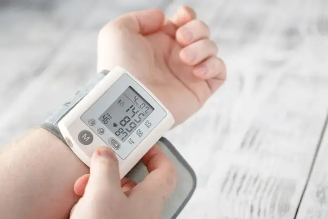 Dłoń z założonym ciśnieniomierzem nadgarstkowym pokazującym wynik 145/87 mmHg i puls 46/min.
