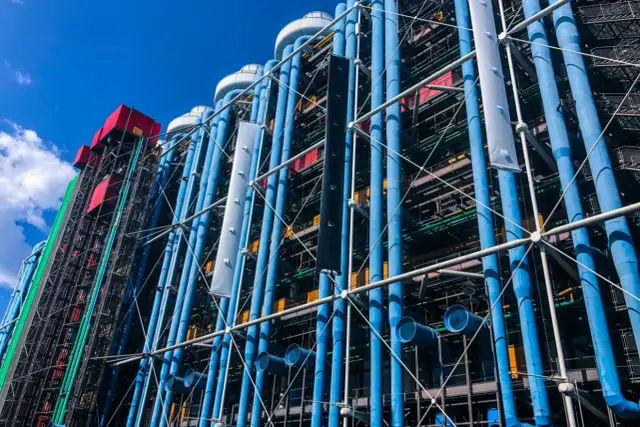 Centrum Pompidou w Paryżu z błękitnymi rurami i kolorowymi elementami architektonicznymi pod błękitnym niebem.