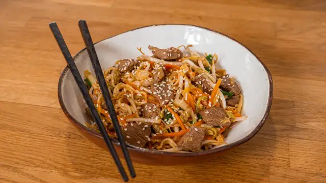 Makaron Chow Mein z wołowiną, warzywami i sezamem w misce z pałeczkami.