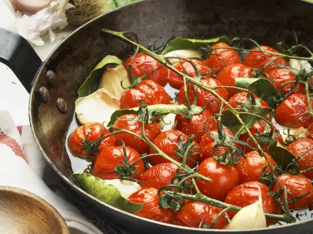 Saftige cherry tomaten mit Knoblauch und Lorbeerblättern in einer Pfanne, bereit zum Garen.