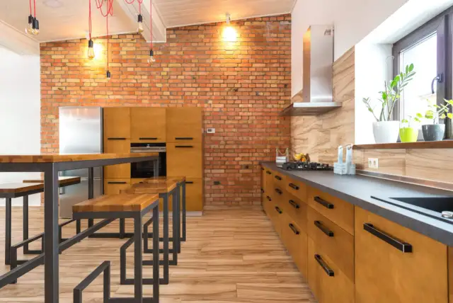 Cocina estilo industrial con pared de ladrillo visto, muebles de madera, encimera oscura y una isla con bancos.
