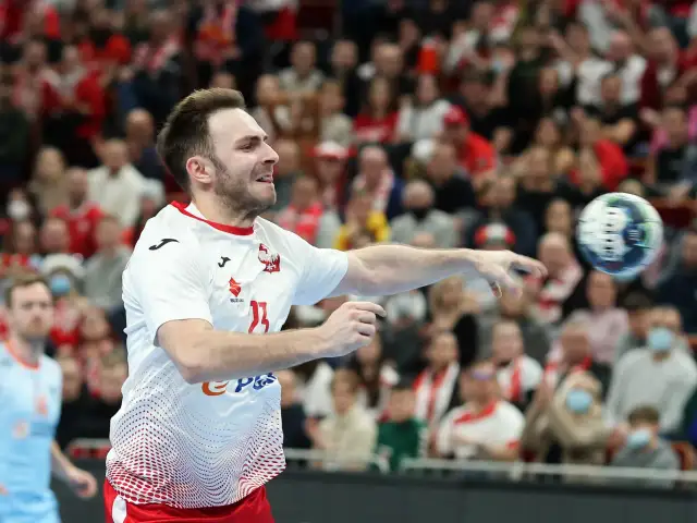 Piłkarz ręczny Polski w akcji, rzuca piłkę. W tle widać trybuny z kibicami, którzy dopingują swoją drużynę w meczu przeciwko Iranowi.