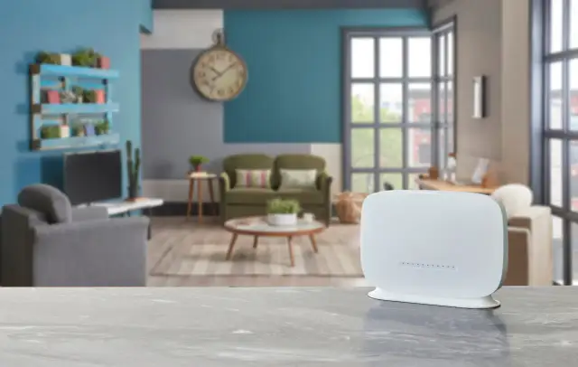 Biały router na blacie, w tle salon z kanapami i zegarem. Zastanawiasz się qos co to? To jakość usług, kluczowa dla płynnego internetu.