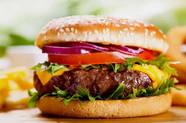 Soczysty burger z serem, pomidorem, czerwoną cebulą i sałatą na bułce z sezamem.