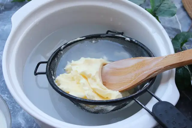 Proceso para como hacer mantequilla casera: se lava la mantequilla recién hecha en un colador con agua fría, usando una cuchara de madera.