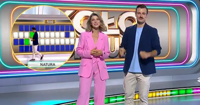 Prowadzący Koło Fortuny na tle planszy z literami i neonowych dekoracji.