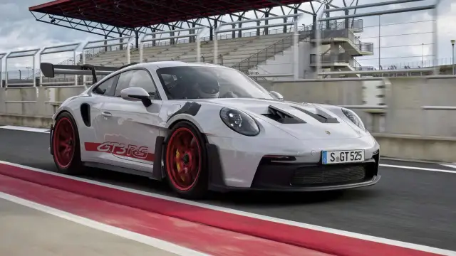 Biały Porsche GT3 RS z czerwonymi felgami i naklejkami na torze wyścigowym.