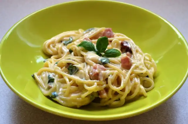 Spaghetti carbonara ze śmietaną, podane w zielonej misce, udekorowane bazylią. Pyszny przepis na klasyczne danie.