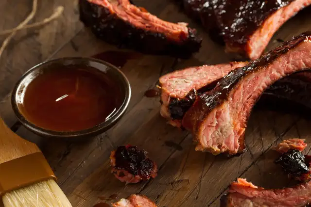Soczyste żeberka w sosie BBQ, obok miseczka z marynatą do żeberek i pędzelek.