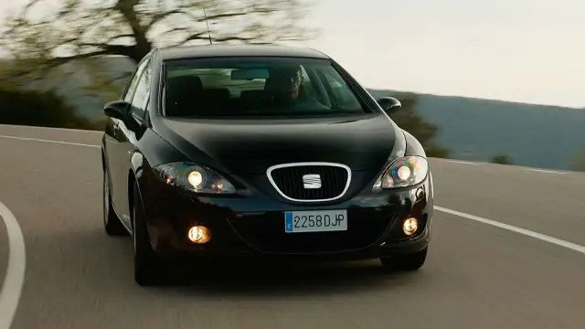 Czarny Seat Leon 2 jedzie po krętej drodze wśród drzew.